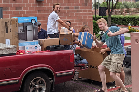 college students unloading boxes from a truck in front of a college dorm