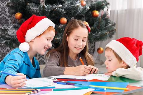 3 children in santa hats writing holiday wish lists with markers